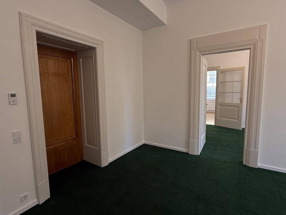 Büro mit grünem Teppichboden, weißen Wänden und Holztüren, das einen klassischen Charme besitzt.
