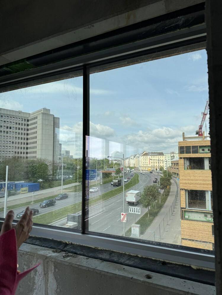 Blick aus einem Fenster auf eine belebte Straße mit Stadtgebäuden und Verkehr unter einem bewölkten Himmel.