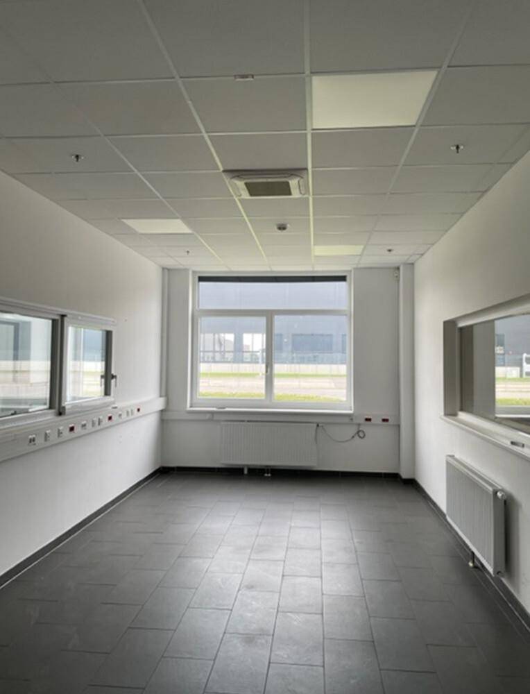 Geräumiger Büroraum mit grauen Fliesen, weißen Wänden und Blick nach draußen durch große Fenster.