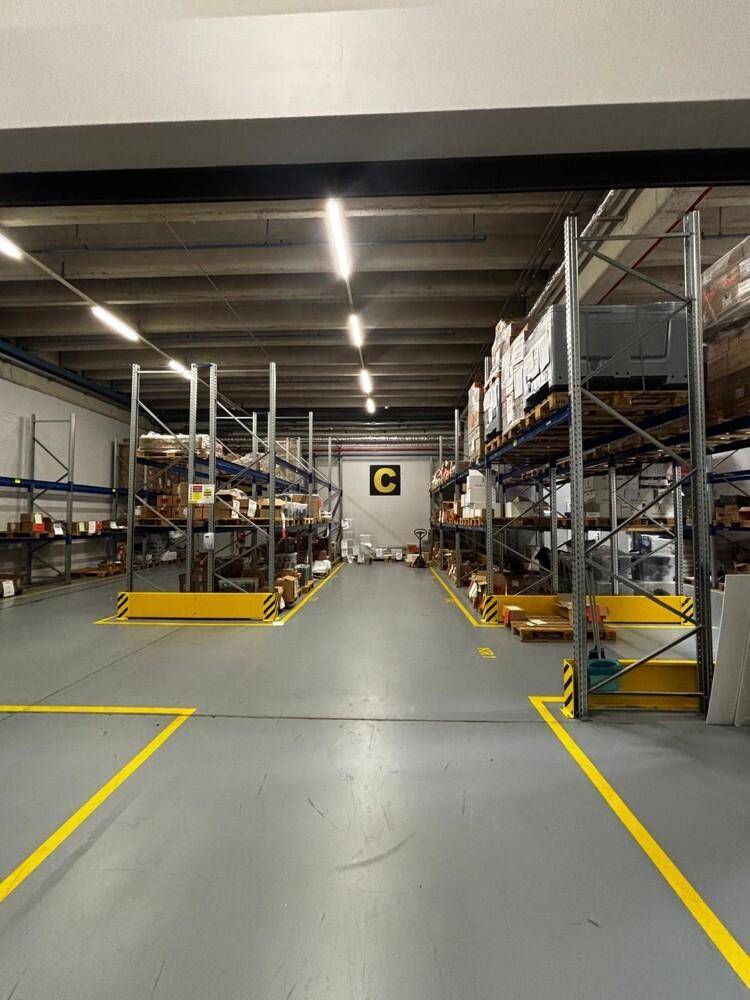 Geräumige Lagerhalle mit hohen Decken, industrieller Beleuchtung und Regalsystemen für die Warenlagerung.