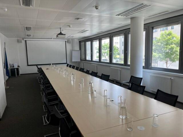 Großer Konferenzraum mit langem Tisch, vielen Stühlen, Beamer und Fenstern mit Blick ins Grüne.
