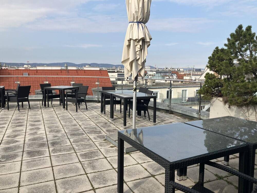 Geräumige Dachterrasse mit Sitzgelegenheiten und einem Sonnenschirm, bietet einen weiten Blick über die Stadt.