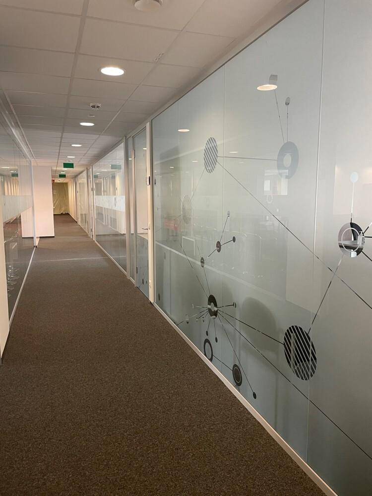 Langer Bürogang mit Teppichboden und Glaswänden, die mit modernen Mustern verziert sind.