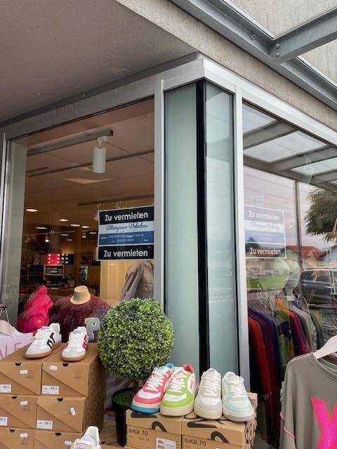 Schaufenster eines Geschäfts mit "Zu vermieten"-Schildern und einer Auslage von Schuhen und Dekoration.