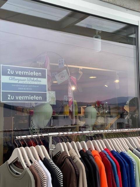 Nahaufnahme eines Schaufensters mit "Zu vermieten"-Schildern und einer Reihe von Kleidungsstücken auf Kleiderbügeln.
