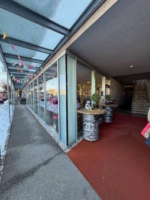 Außenansicht eines Geschäftsgebäudes mit überdachtem Eingangsbereich, großen Glasfenstern und angrenzender Treppe.