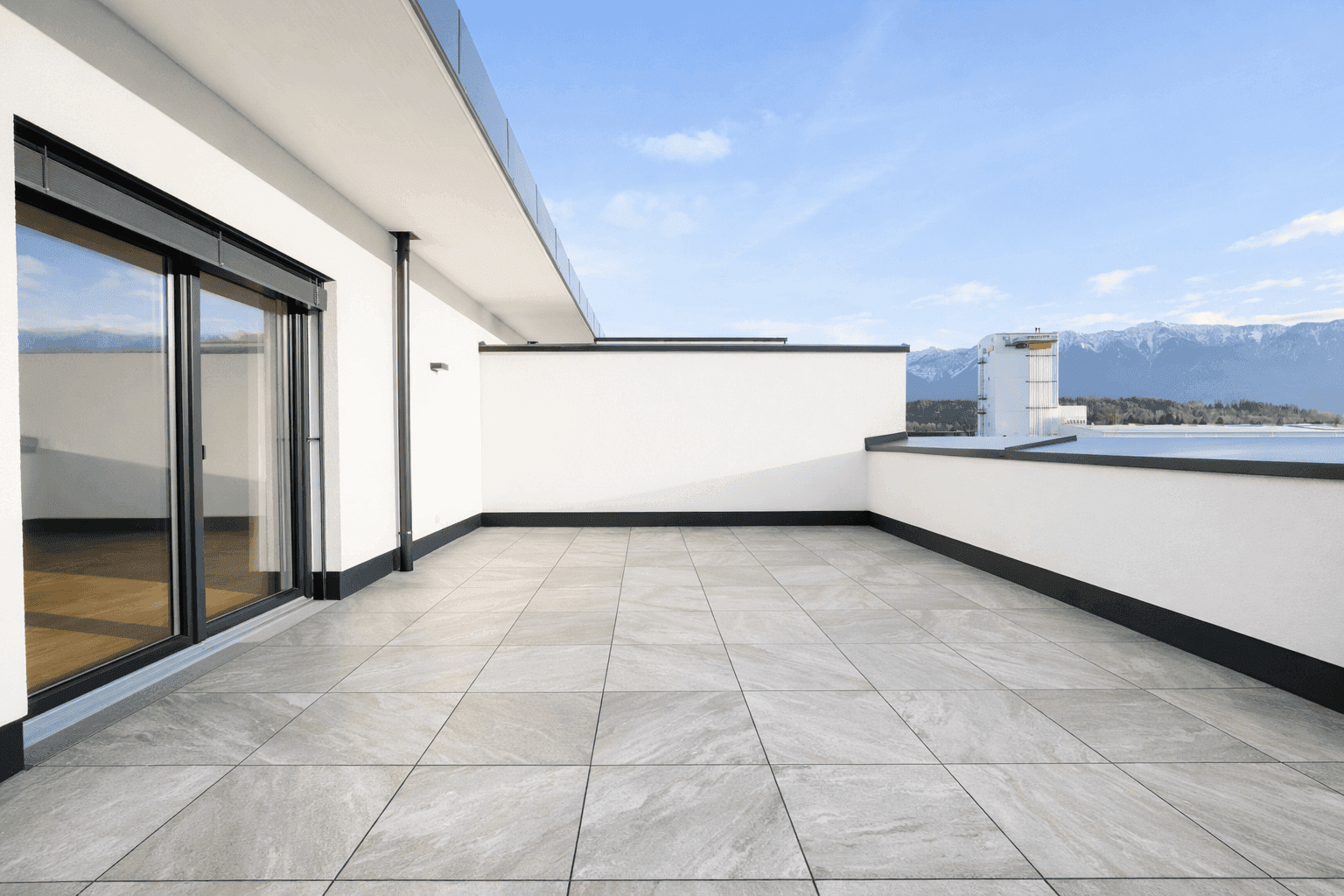 Leere Dachterrasse mit modernen Fliesen und weitem Blick auf die umliegende Berglandschaft.