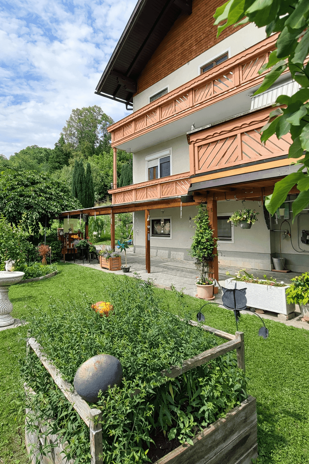 Grüner Gartenbereich mit überdachter Terrasse und Hochbeet neben dem Wohnhaus.