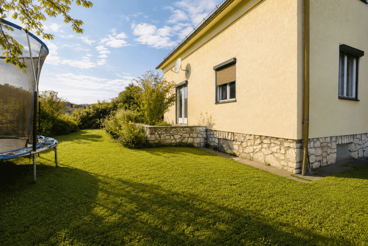 Großer, gepflegter Gartenbereich mit Rasenfläche und Trampolin neben dem Haus.