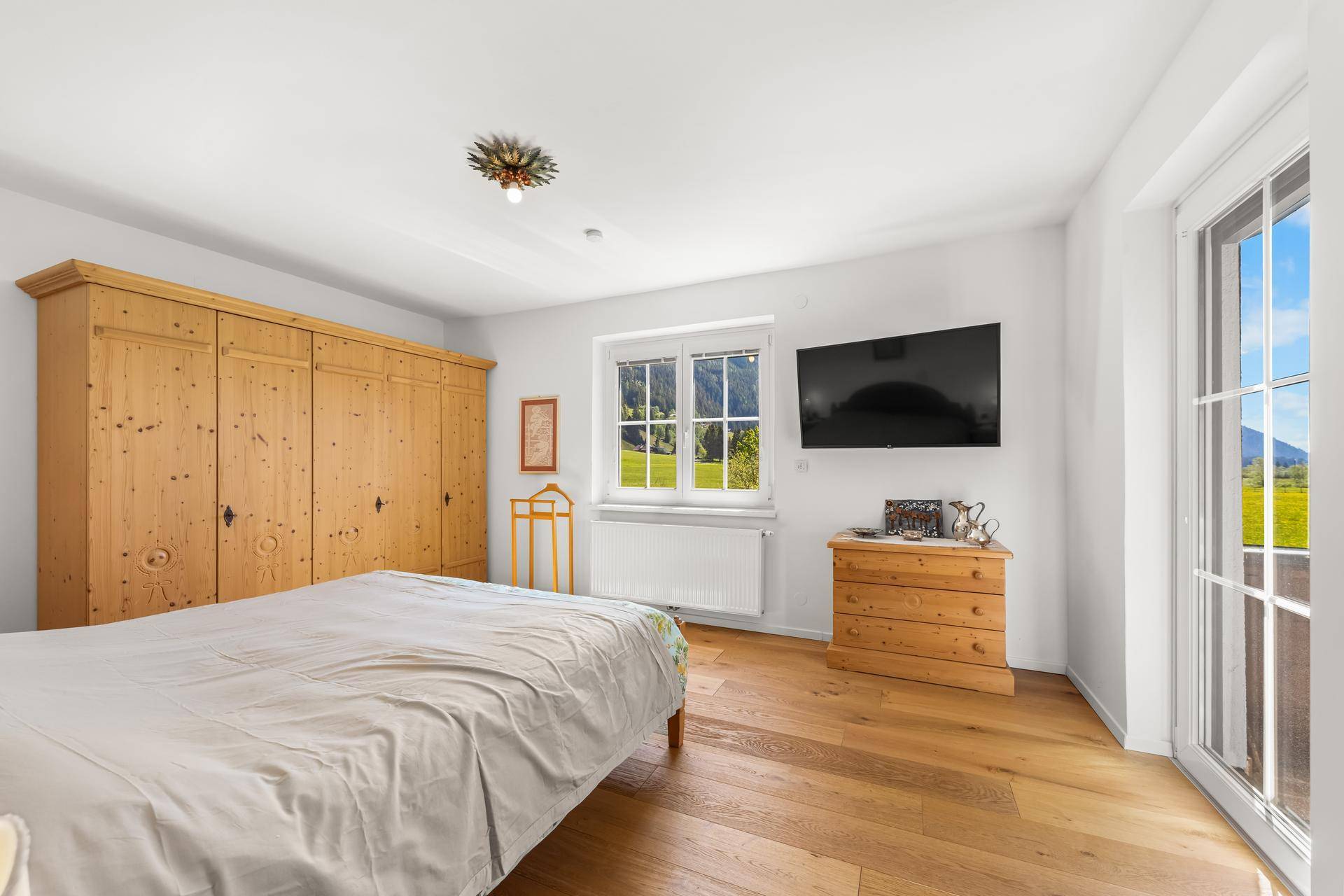 Helles Schlafzimmer mit Holzboden, großem Kleiderschrank und Zugang zu einem Balkon mit Bergblick.
