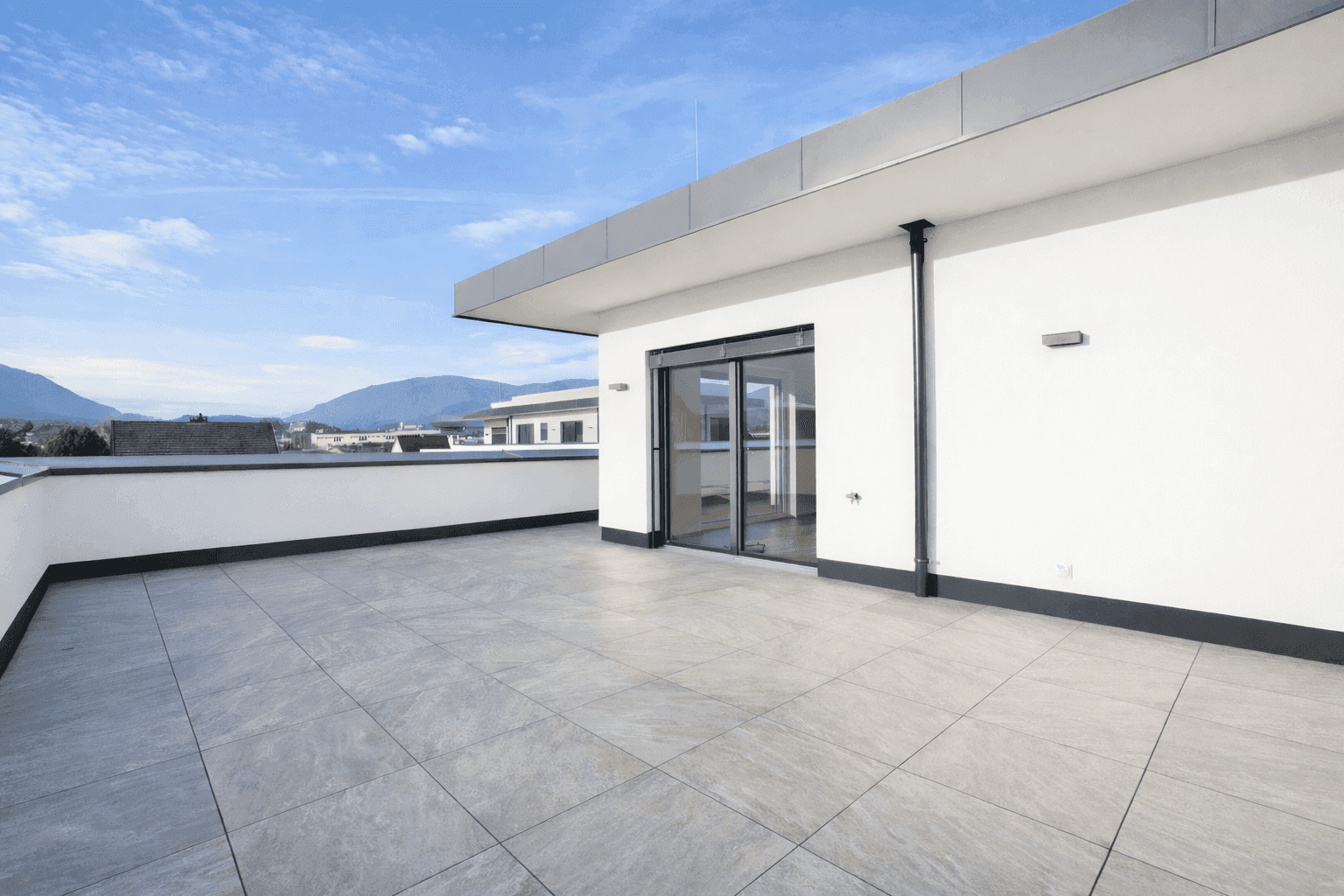Weitläufige Dachterrasse mit modernen Fliesen und Blick auf die umliegende Landschaft.
