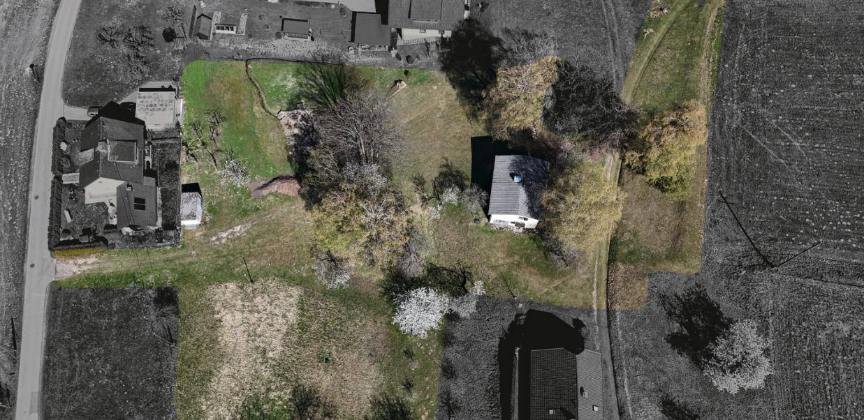 Schwarz-weiß-Luftaufnahme eines Grundstücks mit einem Haus und angrenzenden Feldern, teilweise farbig hervorgehoben.