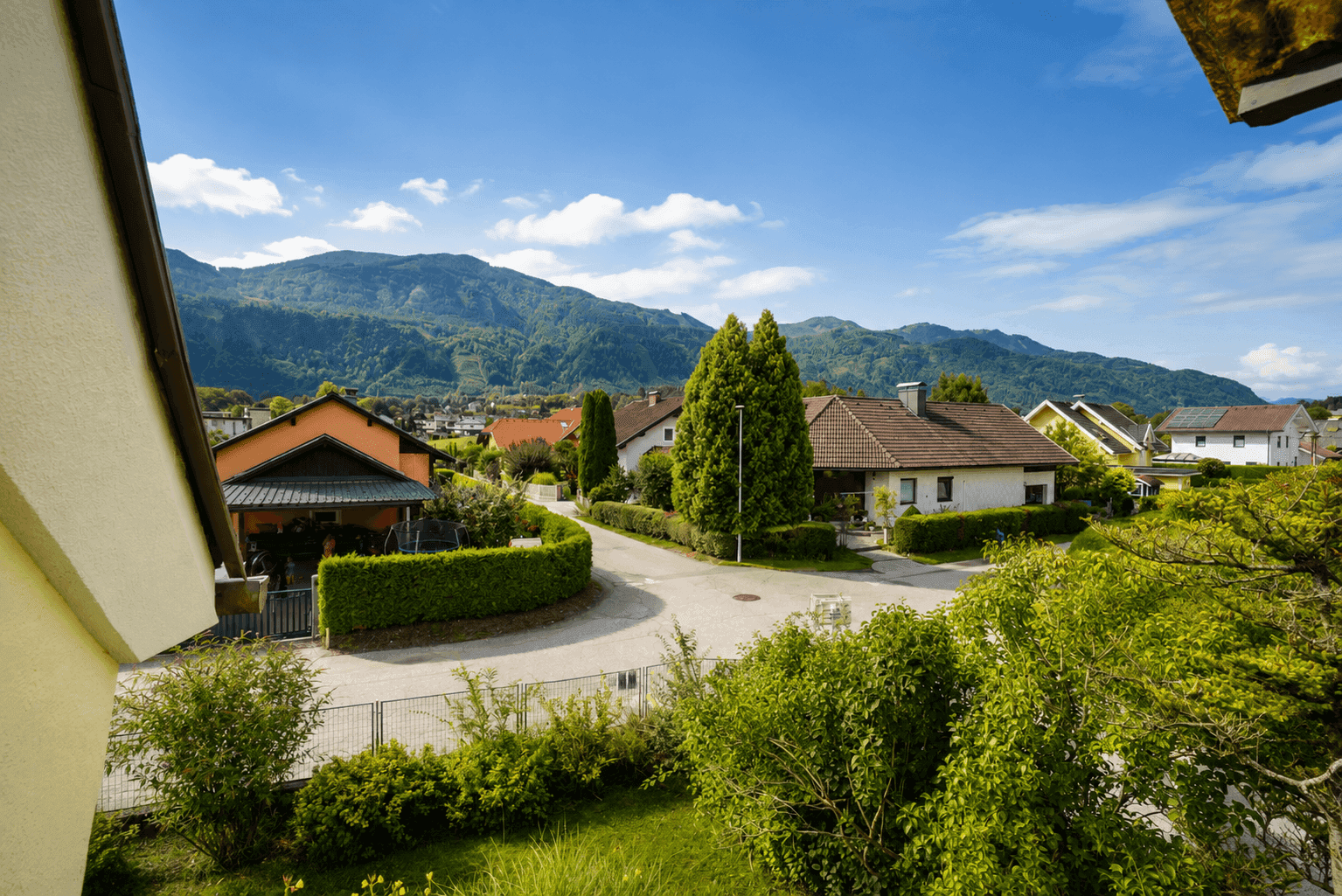 Panoramablick auf eine Wohnsiedlung und die umliegende Berglandschaft von einem Balkon aus.