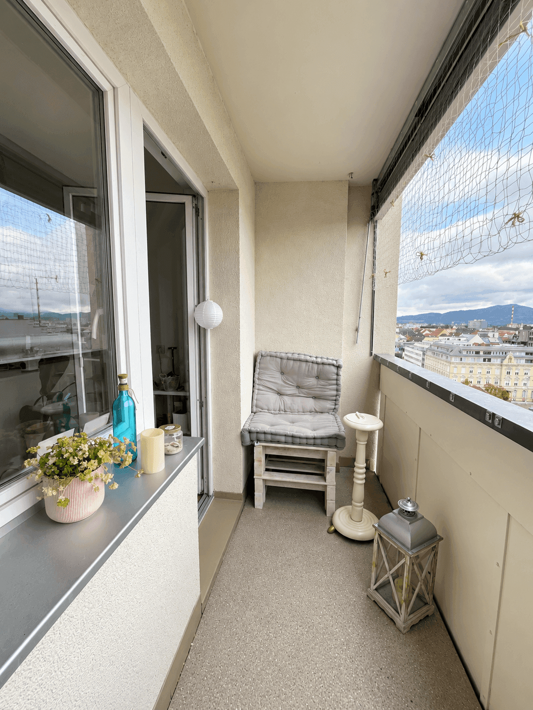 Kleiner Balkon mit Sitzgelegenheit, Dekoration und Blick über die Stadtlandschaft.