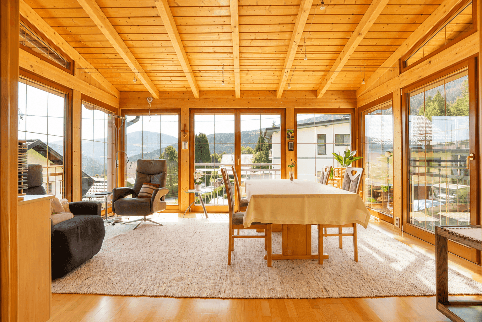 Heller, holzvertäfelter Wohnbereich mit großen Fenstern und Bergblick, ideal zum Entspannen.
