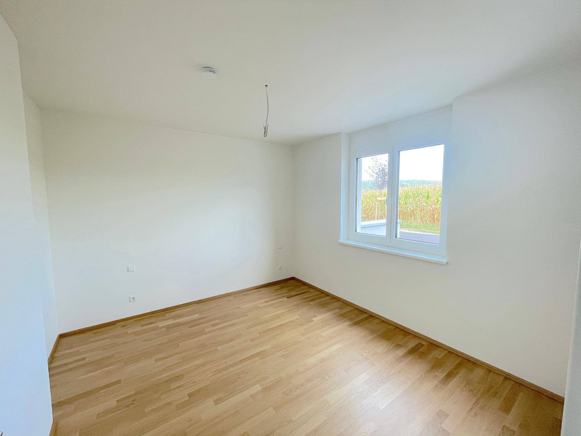 Schlafzimmer mit hellem Holzboden und Fensterblick auf die umliegenden Felder und Natur.