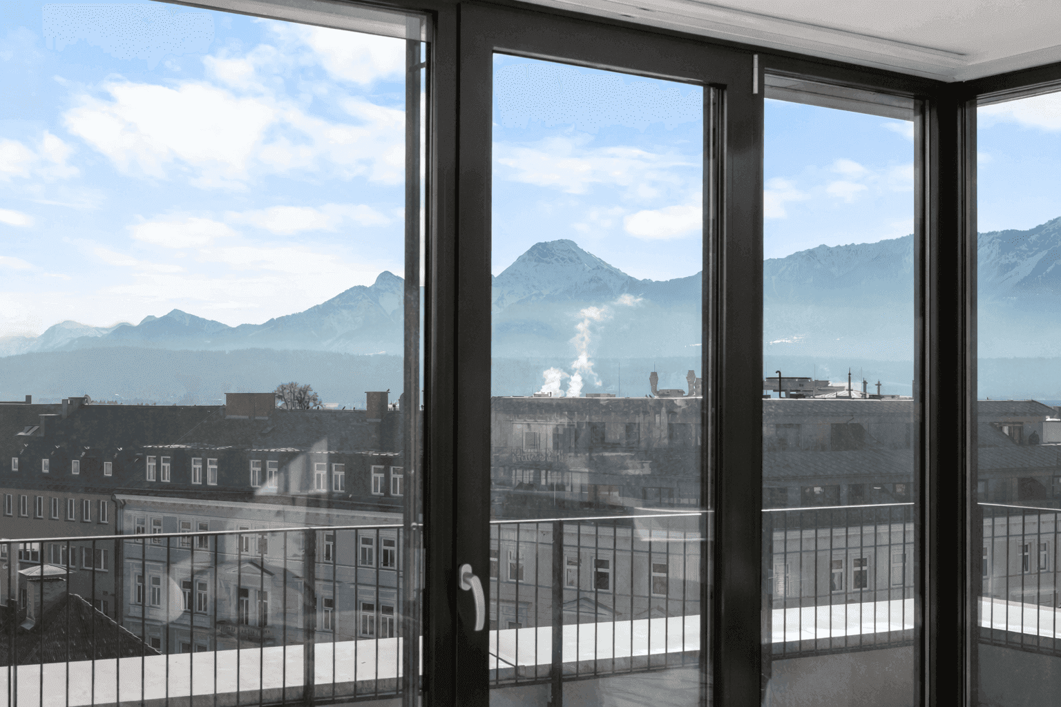 Panoramablick auf die schneebedeckten Berge und die Stadt durch raumhohe Fenster.
