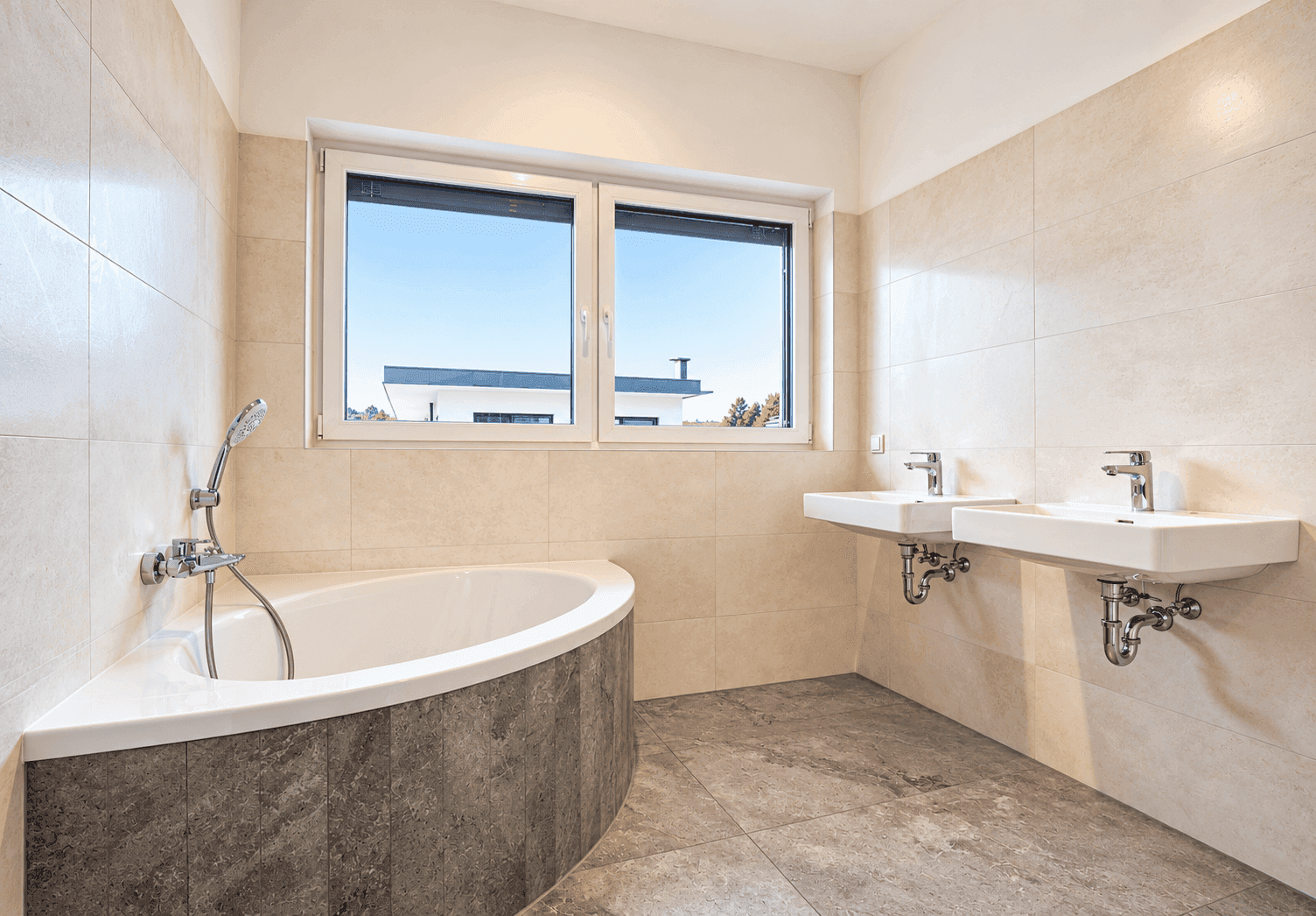 Helles Badezimmer mit Badewanne, zwei Waschbecken und Fenster, komplett gefliest.