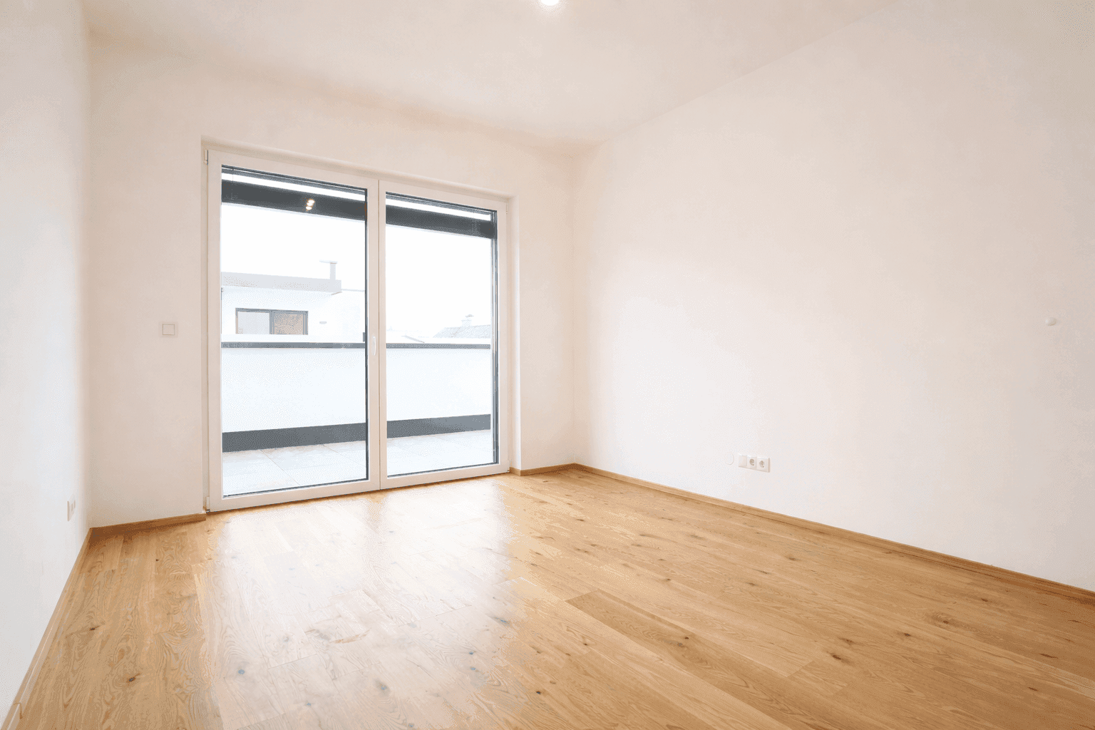 Helles, leeres Schlafzimmer mit Parkettboden und direktem Zugang zu einem Balkon.