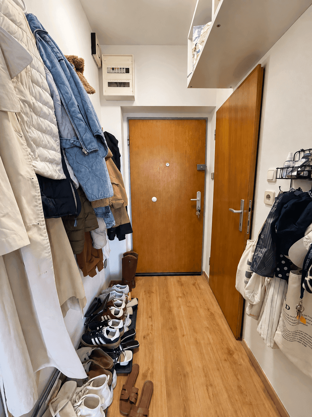 Eingangsbereich mit Garderobe, vielen Schuhen und einem Sicherungskasten an der Wand.
