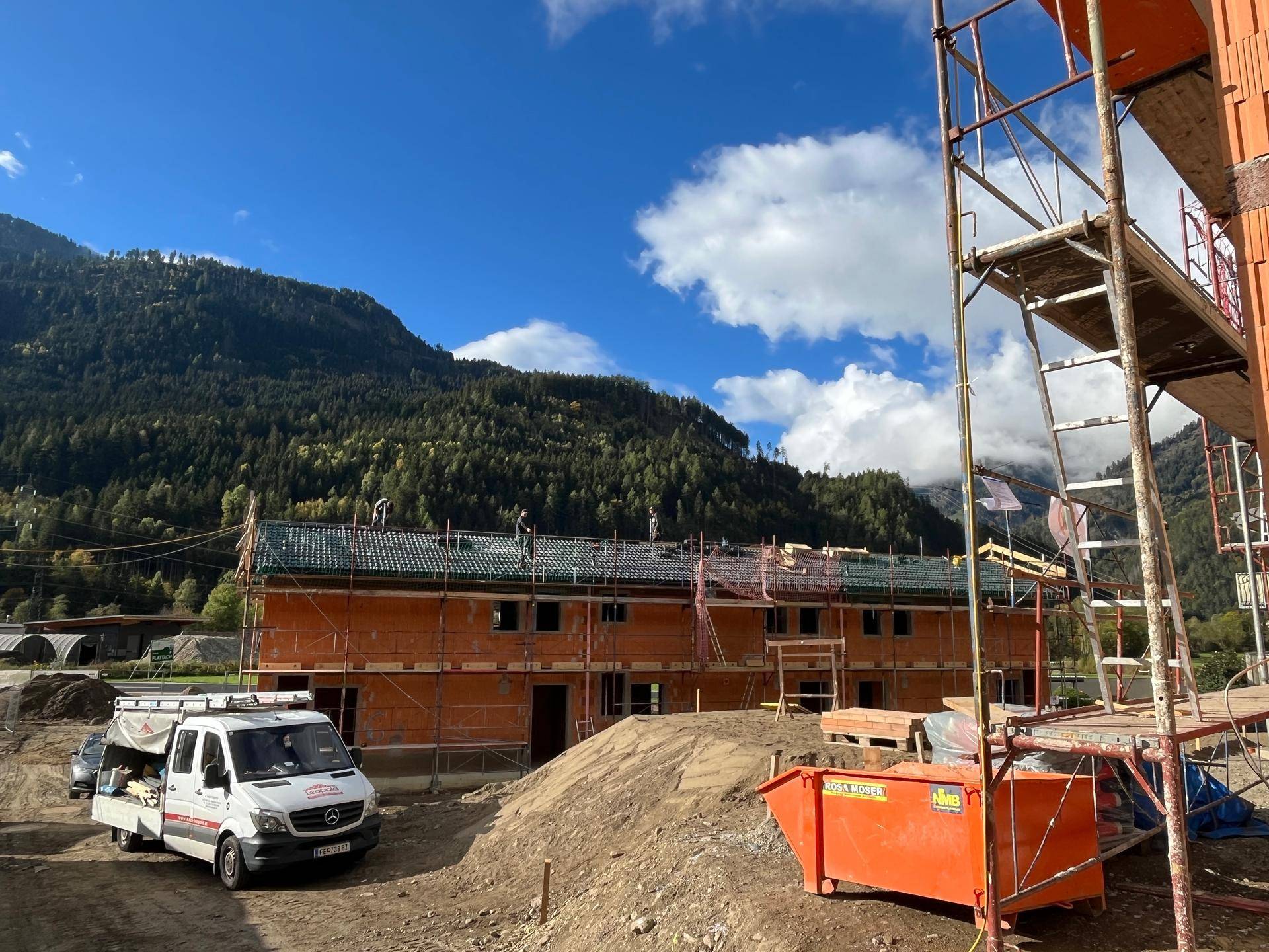 Fortgeschrittenes Neubauprojekt mit bereits gedecktem Dach und Gerüsten vor einer beeindruckenden Berglandschaft.