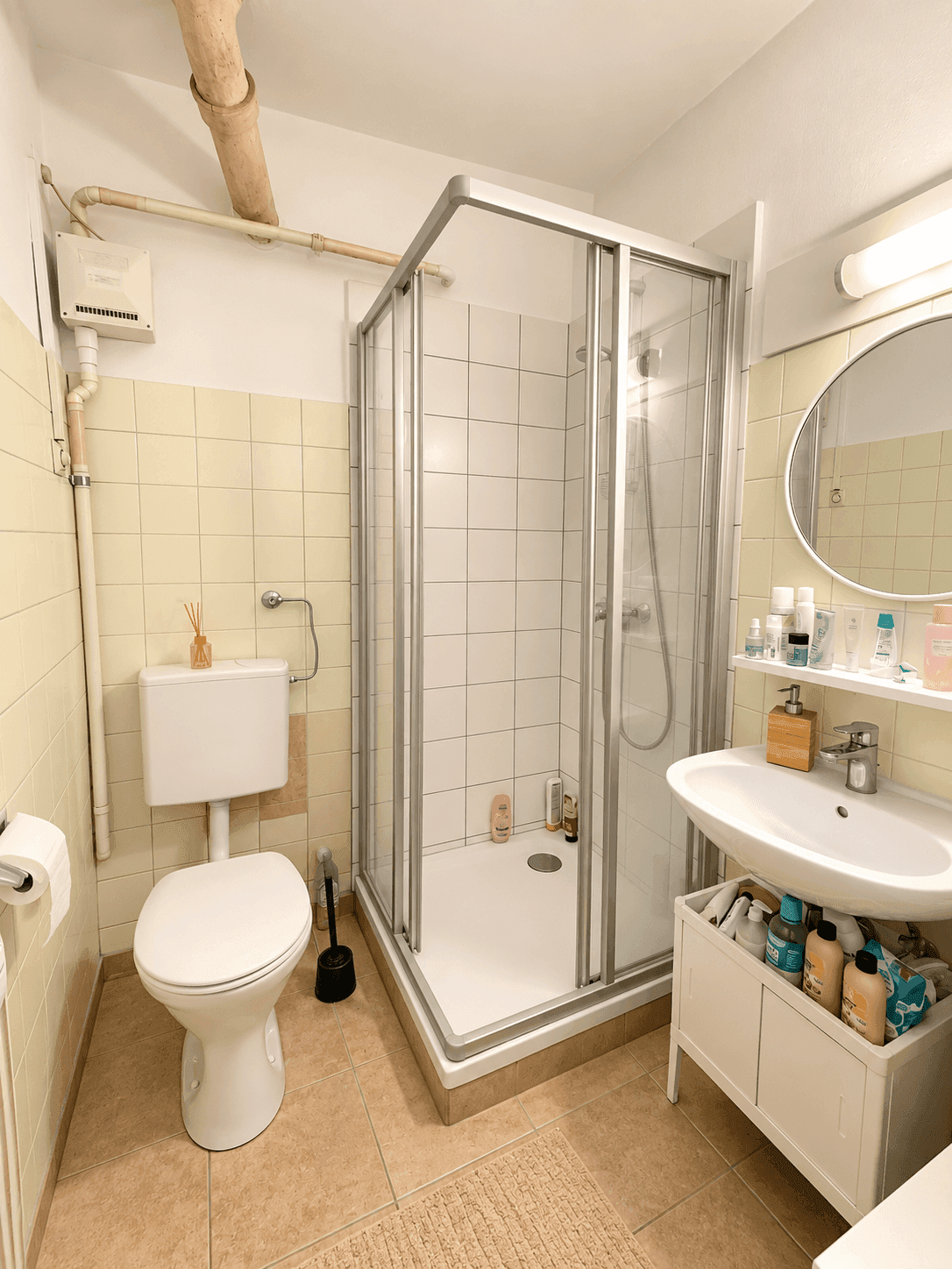 Badezimmer mit Duschkabine, WC, Waschbecken und hellgelben Fliesen an den Wänden.