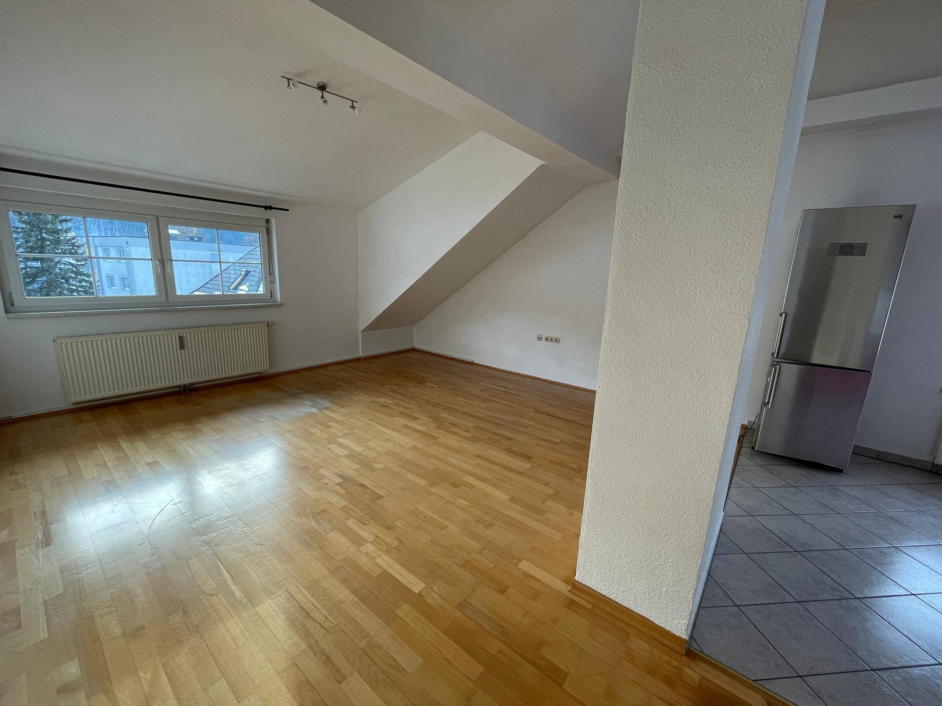 Heller Wohnbereich mit Holzboden, weißen Wänden und schrägen Decken, bereit zur individuellen Gestaltung.