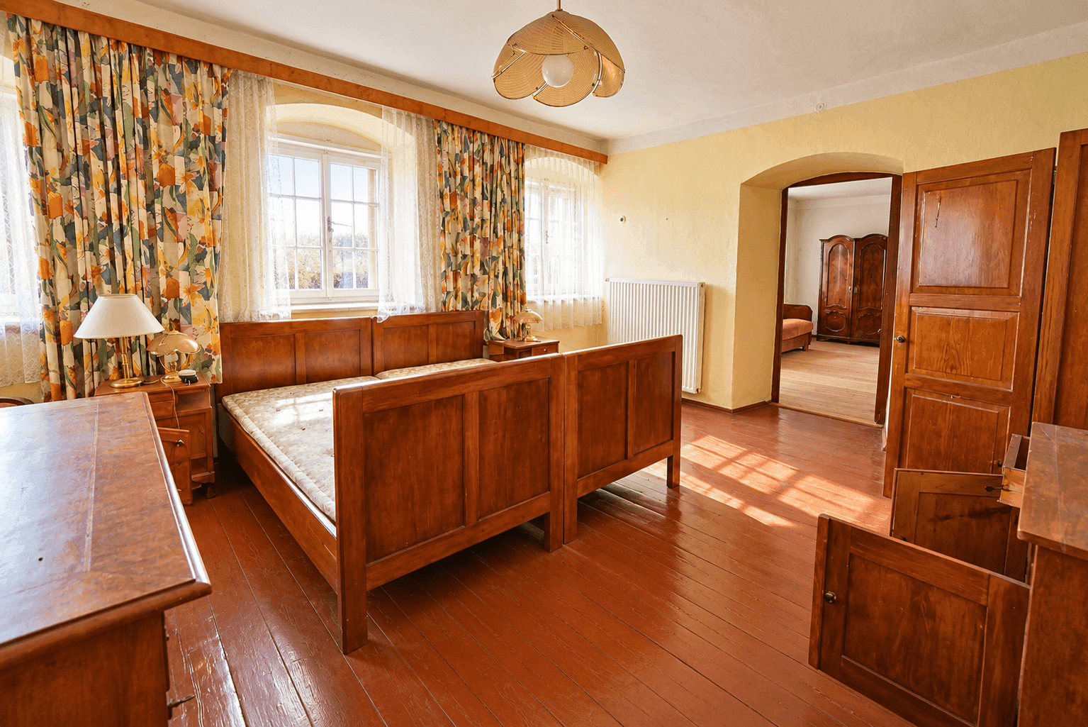 Helles Schlafzimmer mit Holzdielenboden und traditionellen Holzmöbeln, mit Blick ins Grüne.