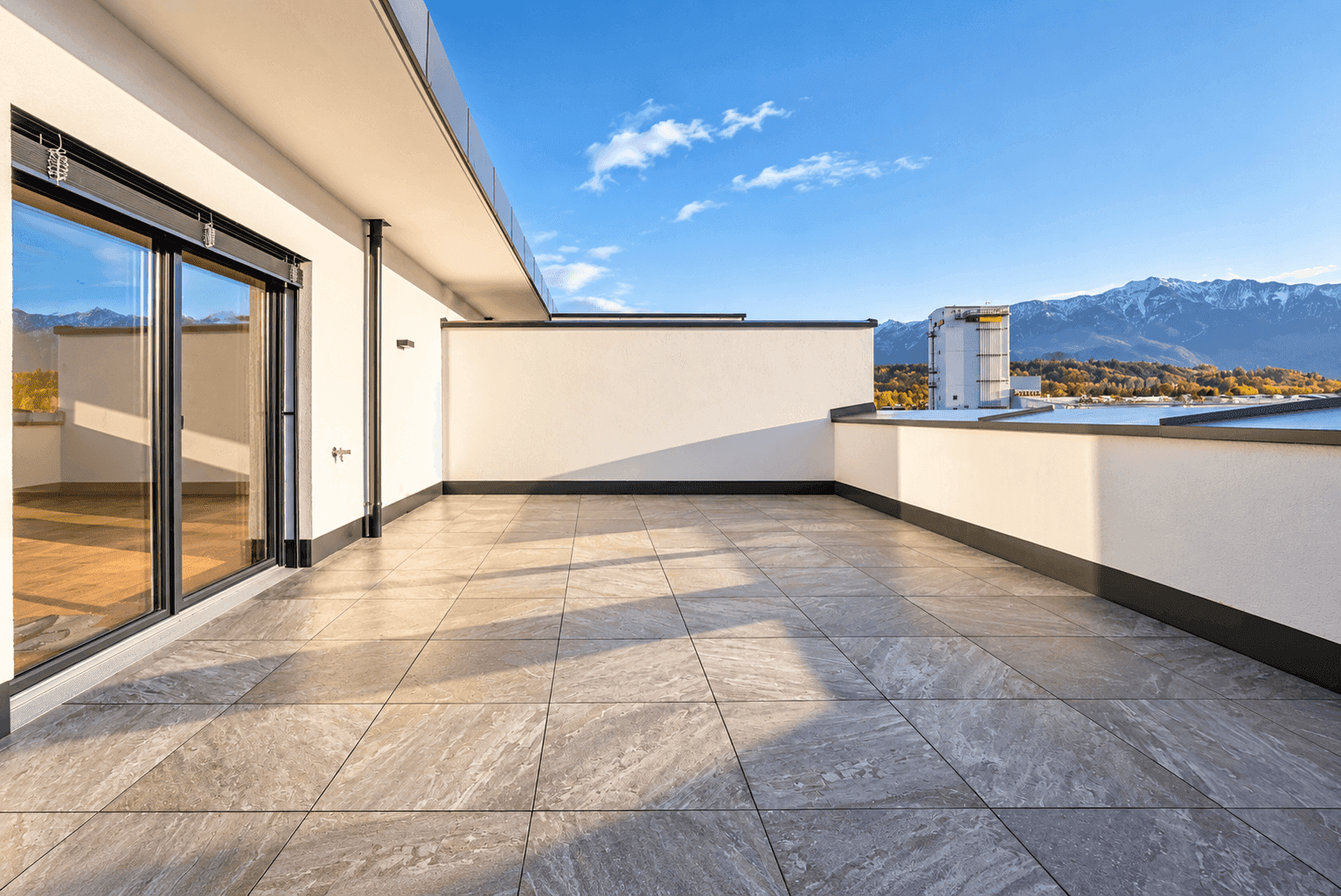 Geräumige, unmöblierte Dachterrasse mit Fliesenboden und weitem Blick auf die Berge.