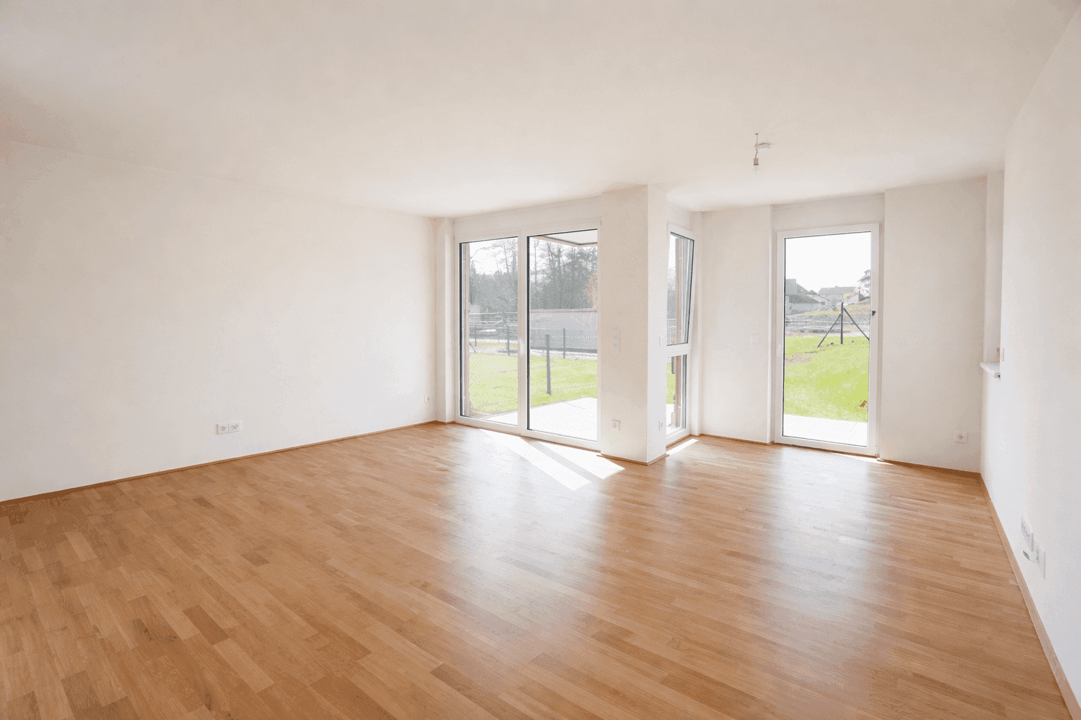 Geräumiges Wohnzimmer mit hellem Parkettboden, großen Fenstern und Zugang zum Garten.
