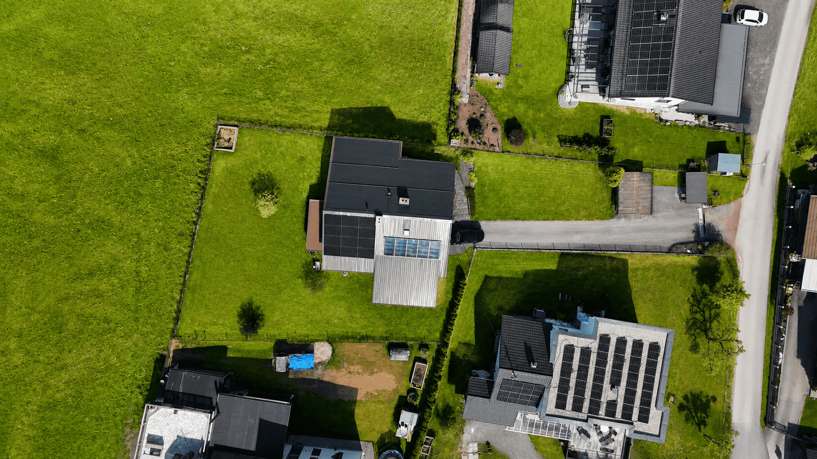 Luftaufnahme von Wohnhäusern mit Solaranlagen auf den Dächern, umgeben von grünen Wiesen.