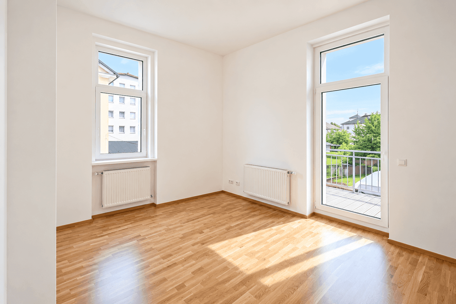 Helles Zimmer mit Parkettboden, Fenster und direktem Zugang zum Balkon.