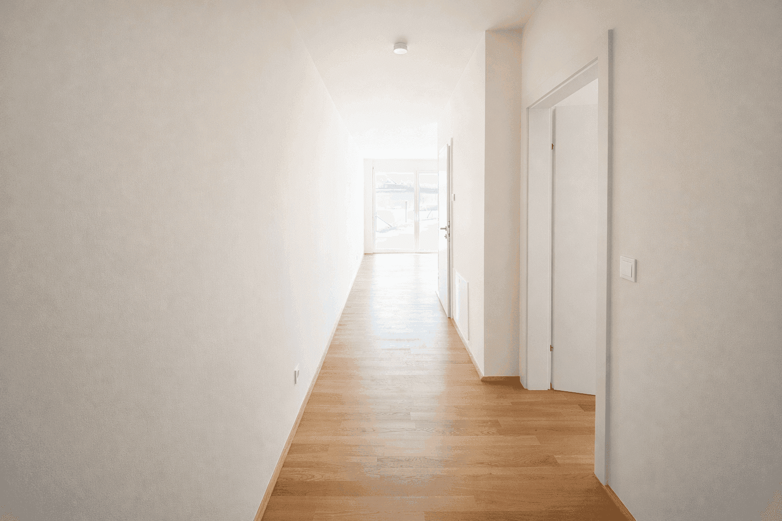 Heller Flur mit Holzparkettboden, weißen Wänden und viel natürlichem Licht am Ende.