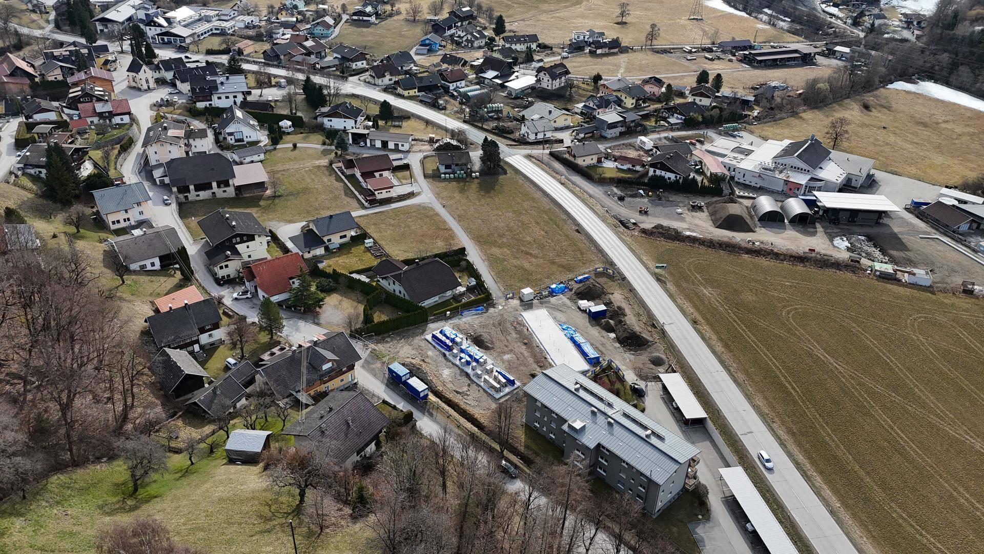 Luftaufnahme einer ländlichen Siedlung mit Häusern, Feldern und Berglandschaft.