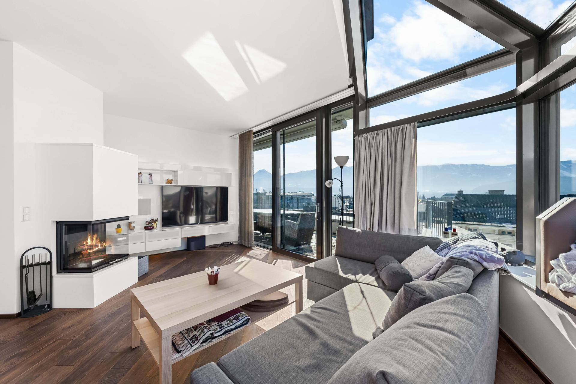 Gemütliches Wohnzimmer mit Kamin, Holzboden und großen Fenstern mit Blick auf die Umgebung.
