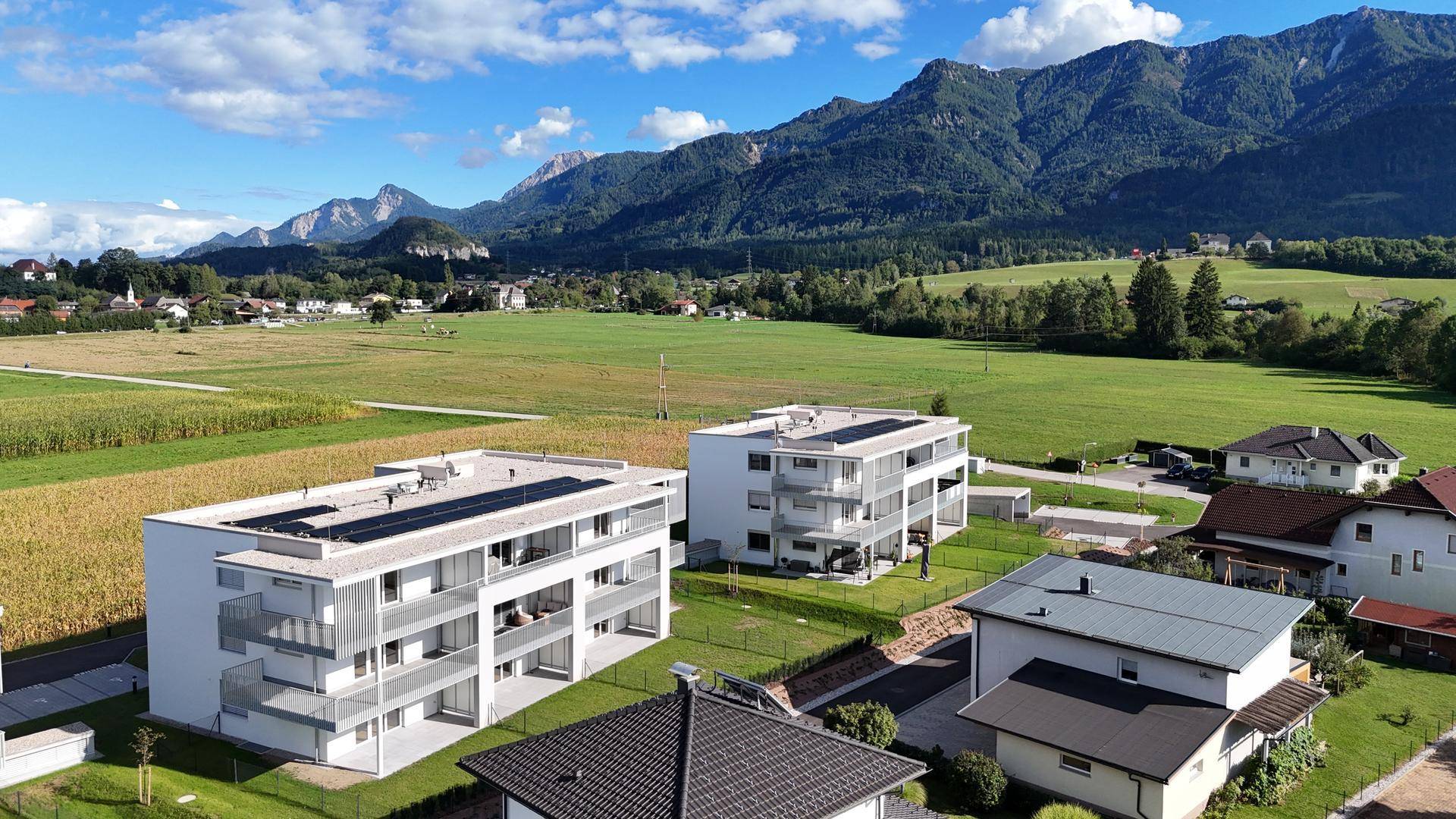 Luftaufnahme von zwei modernen Wohngebäuden in einer grünen, ländlichen Umgebung mit Bergblick.