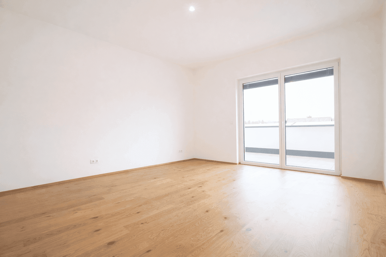 Leeres Schlafzimmer mit hellem Parkettboden und Zugang zu einem französischen Balkon.
