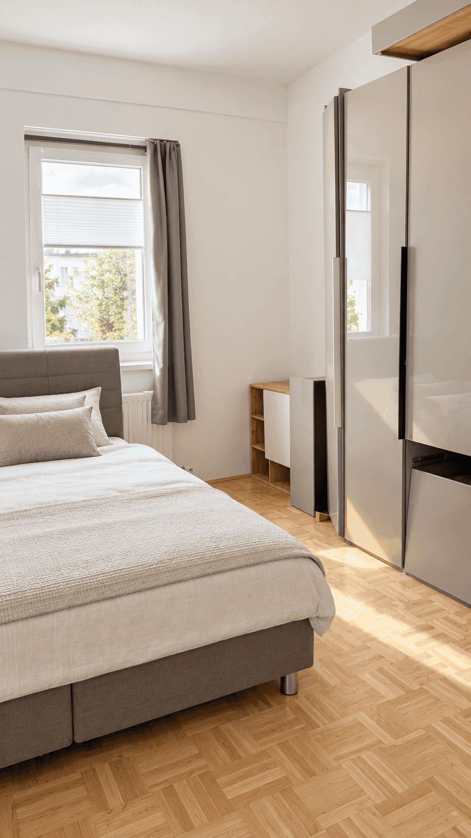 Helles Schlafzimmer mit Parkettboden, großem Fenster und modernem Kleiderschrank.