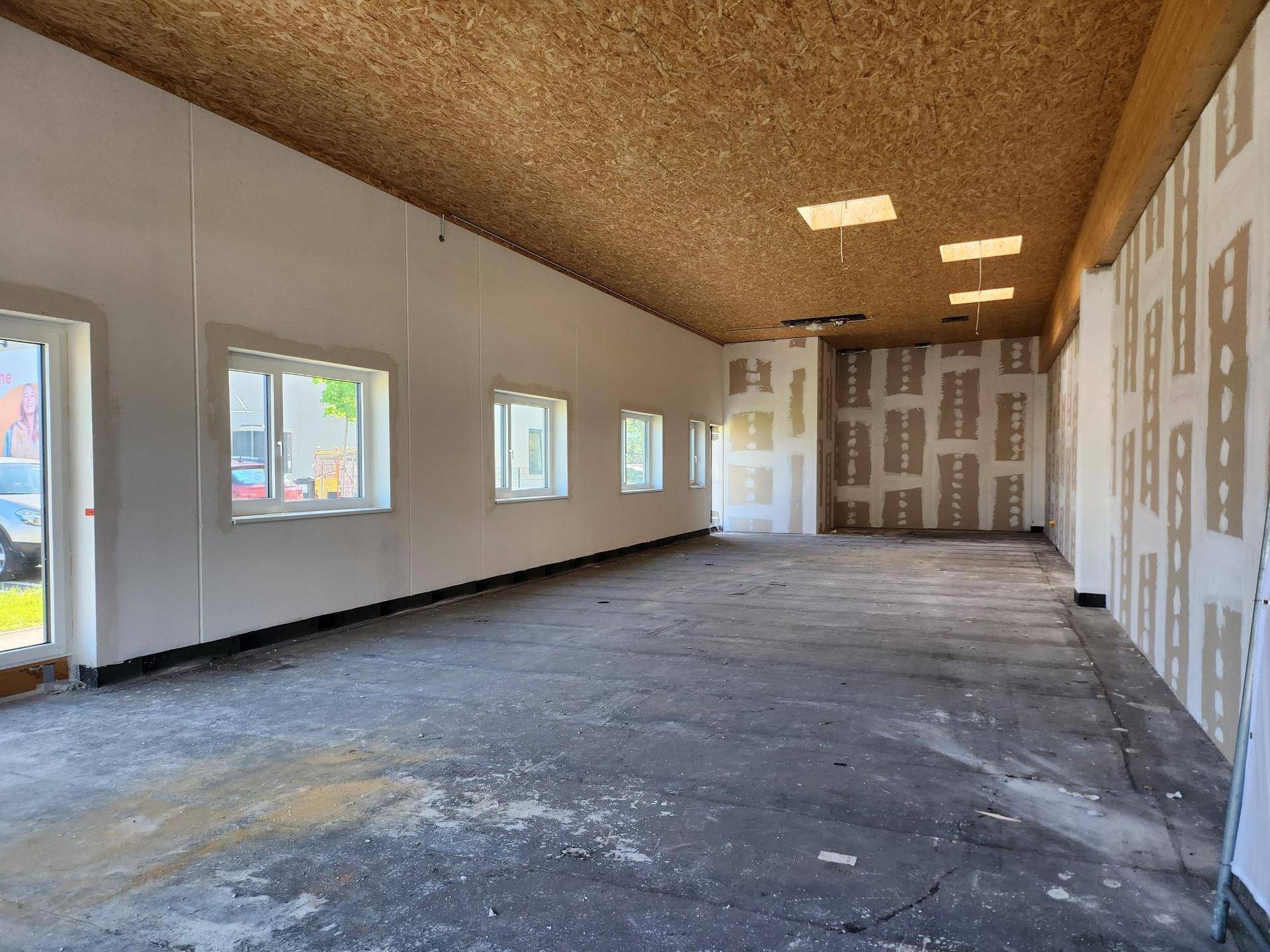 Großer, leerer Innenraum eines Geschäfts mit OSB-Decke und unfertigen Wänden, bereit für den Ausbau.