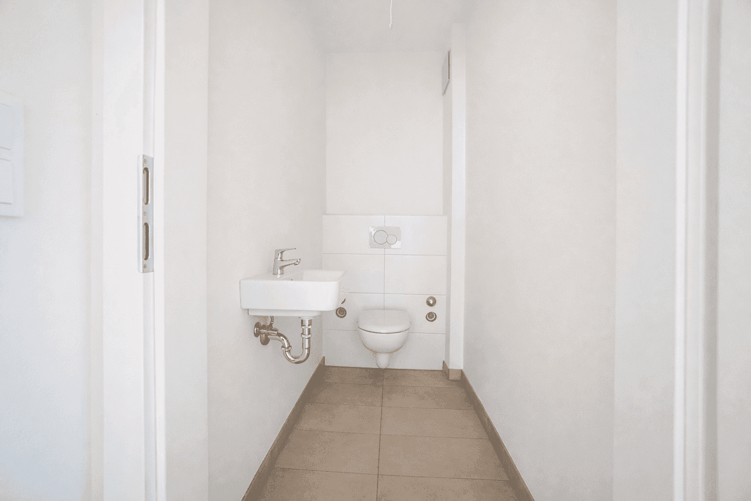 Separates Gäste-WC mit wandhängender Toilette und kleinem Waschbecken in minimalistischem Design.