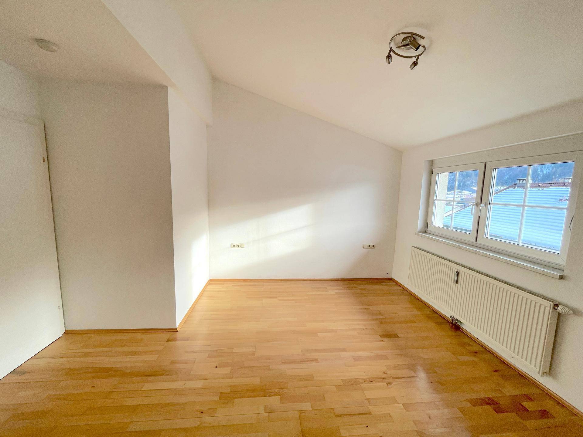 Gemütliches Zimmer mit Holzboden, weißen Wänden und schräger Decke, ideal als Schlaf- oder Arbeitszimmer.