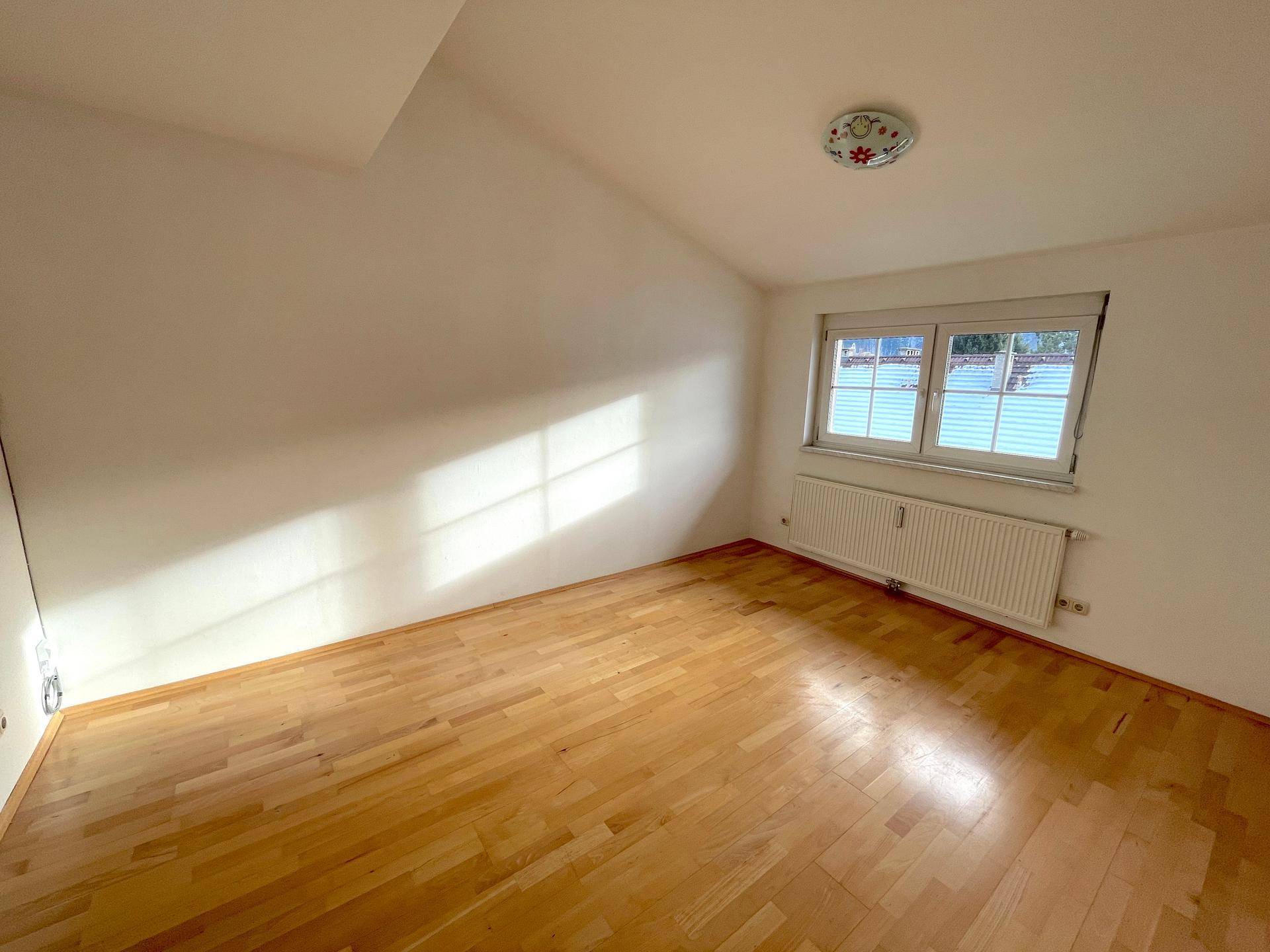 Ruhiges Zimmer mit Holzboden, schräger Decke und Fenster mit Jalousien für Privatsphäre.