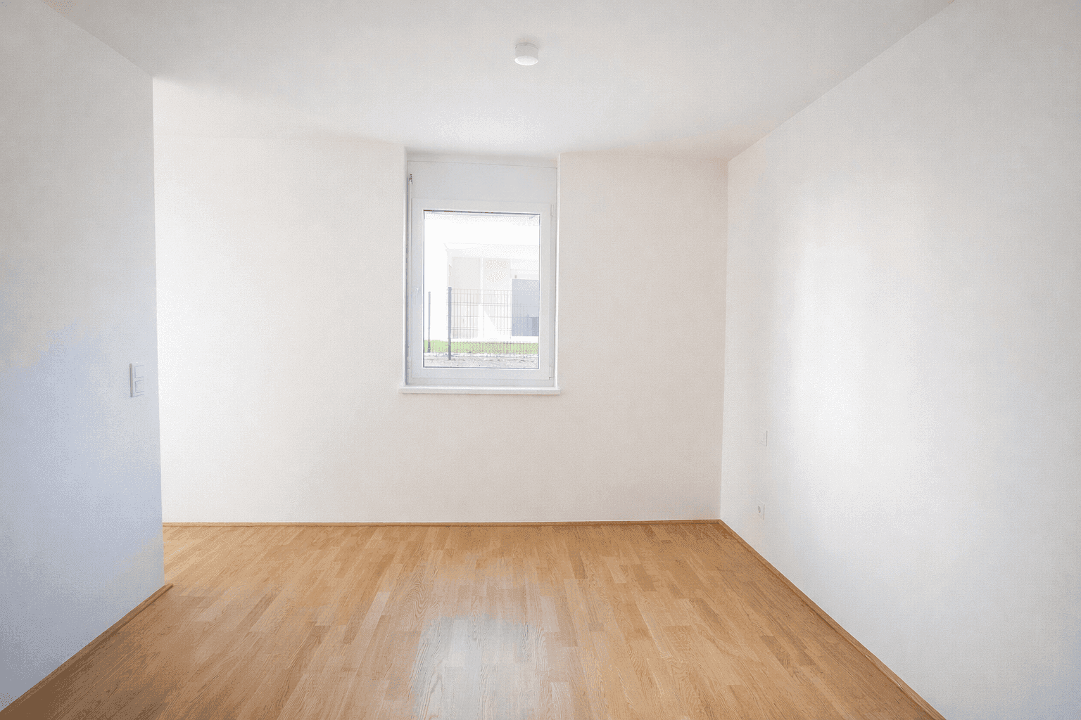 Helles Zimmer mit Parkettboden und einem Fenster, das viel Tageslicht hereinlässt.