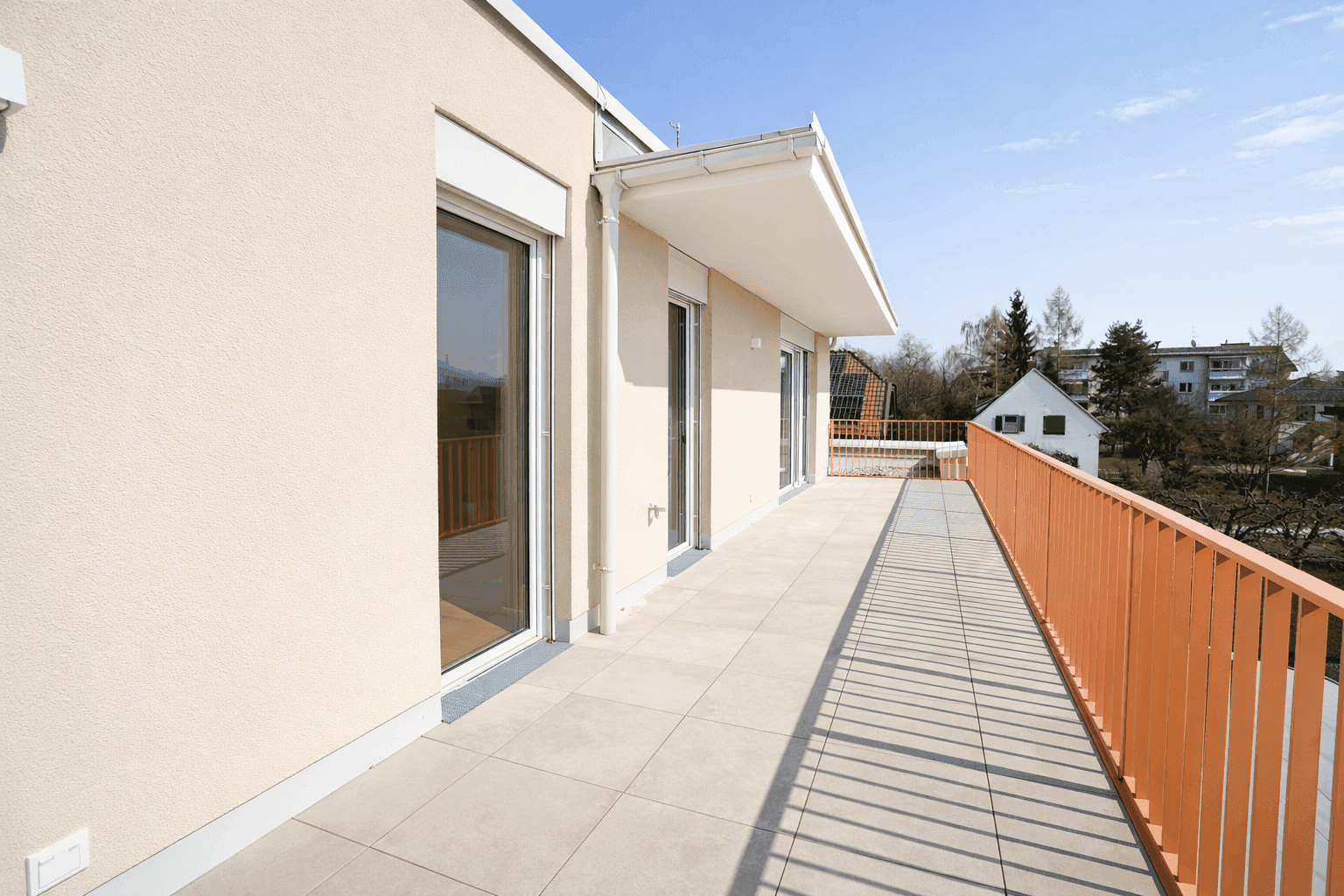 Weitläufige, geflieste Terrasse mit orangefarbenem Geländer und viel Sonnenlicht, ideal zum Entspannen.