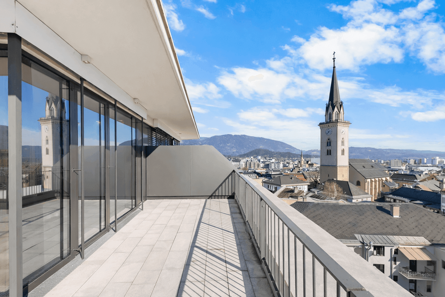 Geräumige Terrasse mit Fliesenboden und Panoramablick auf die Stadt und die Kirchturmspitze.