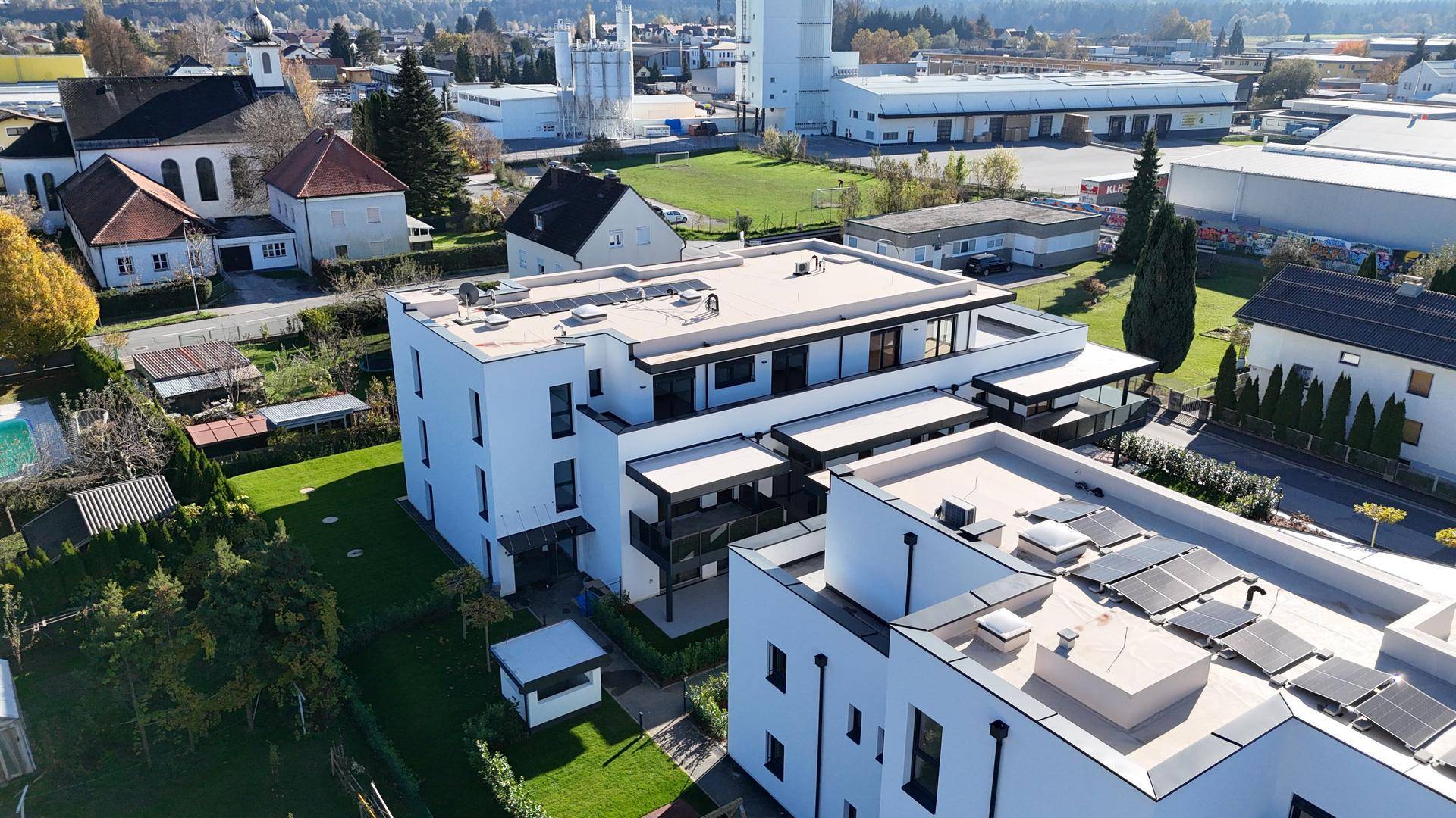 Luftaufnahme einer modernen Wohnanlage mit Photovoltaikanlage auf dem Dach und umliegender Bebauung.