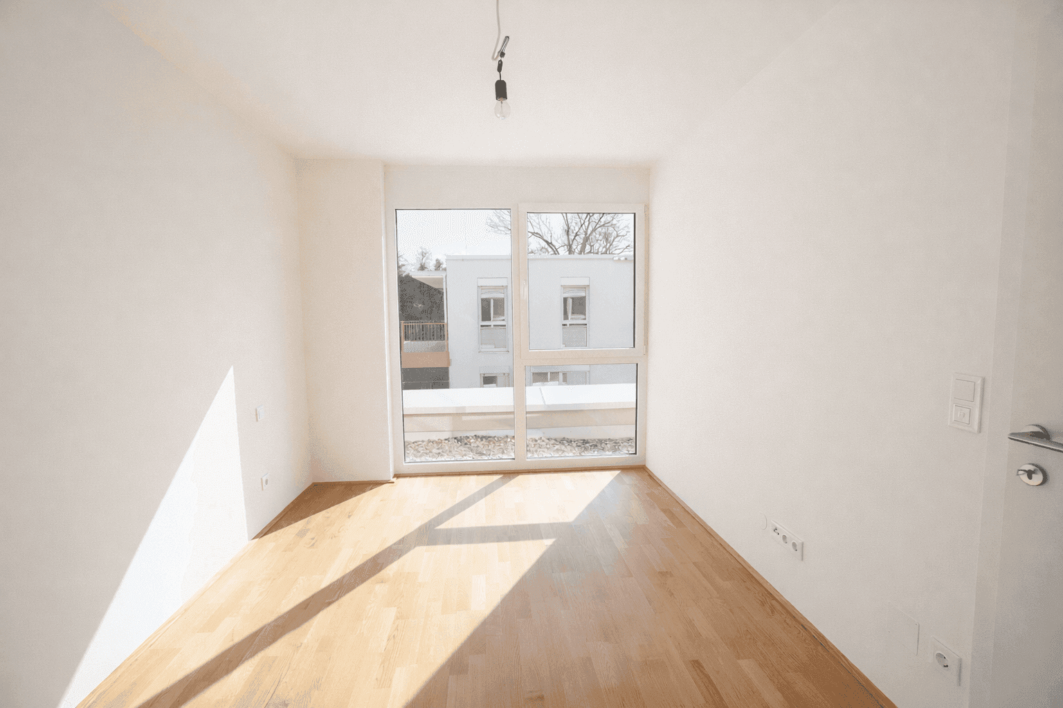 Helles Zimmer mit Parkettboden und großem Fenster, das viel Tageslicht hereinlässt.