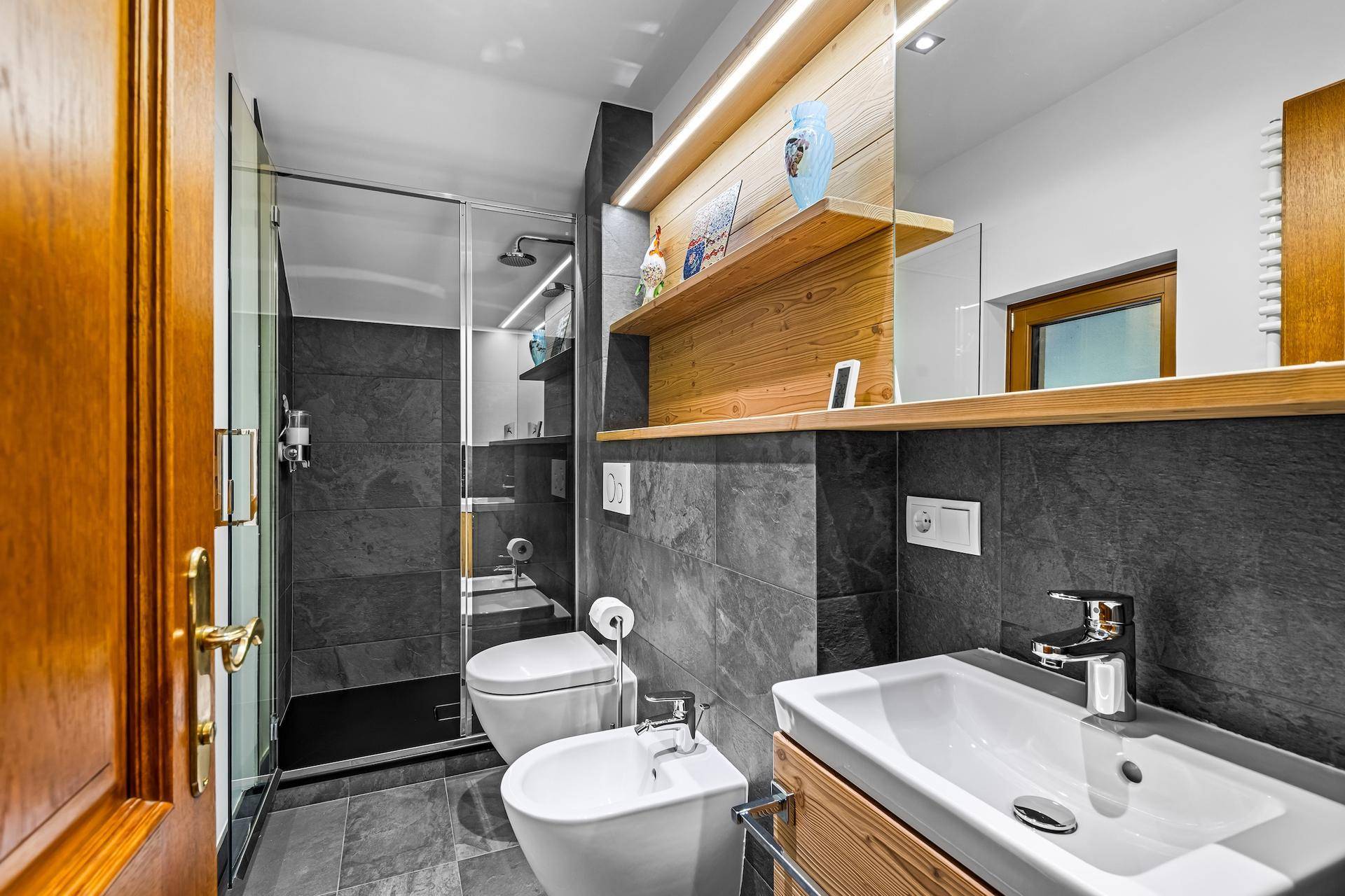 Modernes Badezimmer mit Dusche, Bidet und Waschbecken, ausgestattet mit dunklen Fliesen.