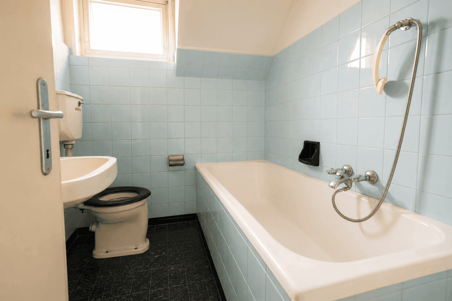 Badezimmer im Stil der 80er Jahre mit hellblauen Fliesen, Badewanne und Fenster.