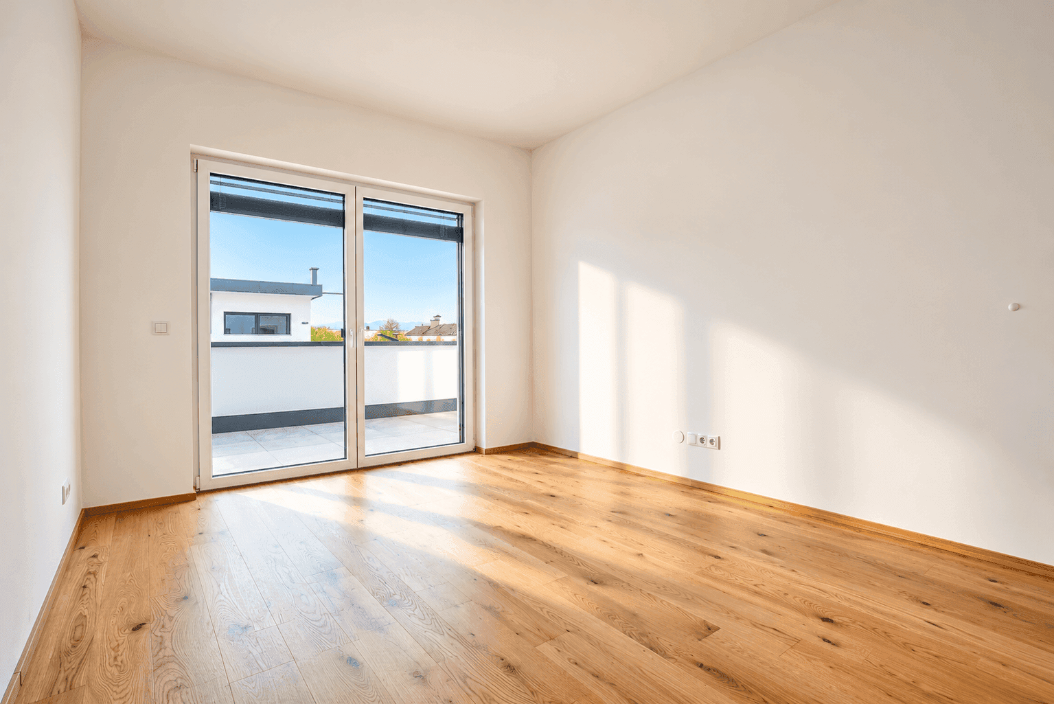 Leeres Schlafzimmer mit Holzboden und Zugang zu einem Balkon oder einer Terrasse.